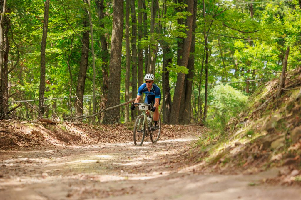 A cyclists rides on a rough dirt road through the forest.